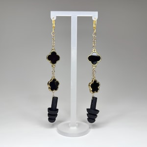 May include: A pair of black and gold earrings with a clover design and black silicone earplugs hanging from the bottom.