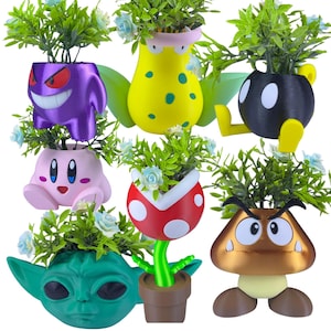 Può includere: Una collezione di vasi a forma di personaggi colorati, tra cui un fantasma viola, una creatura gialla con ali verdi, una bomba nera, un personaggio rosa, una pianta rossa e bianca, un alieno verde e un fungo marrone. Ogni vaso contiene verde e fiori blu.