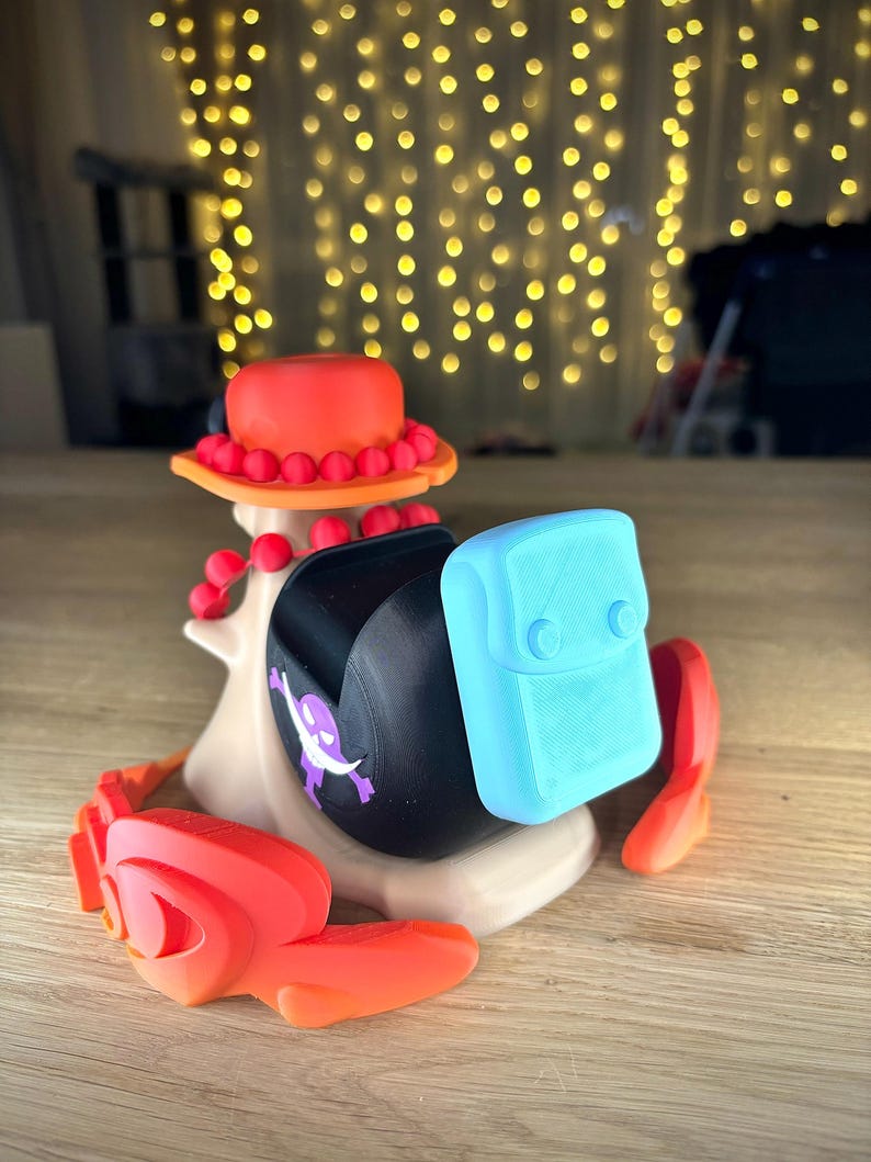 May include: A 3D printed figurine of a character wearing a red and orange hat with a blue and white backpack. The figurine is standing on a wooden surface.