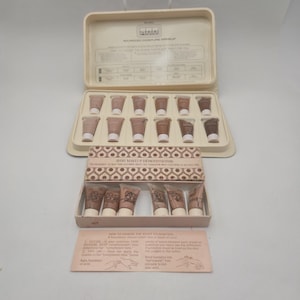 May include: Vintage Avon Advanced Moisture Makeup foundation demonstrator kit. The kit includes a beige plastic case with multiple foundation samples in various shades. The text "AVOID MAKEUP DEMONSTRATOR" is visible.