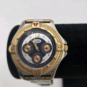 May include: A Guess watch with a silver and gold-tone metal band and case. The watch face is navy blue and white with gold-tone hands and markers. The watch has multiple subdials and the number 12 is at the top.