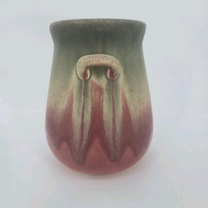 May include: A ceramic vessel featuring a rounded body and a wide opening. The exterior displays a blended glaze with a muted sage green upper section transitioning into a deep rose pink base, characterized by vertical drip-like patterns.