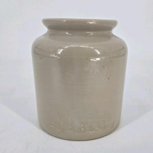 May include: A light beige ceramic jar with a smooth, glossy finish and a wide, rounded rim. The base of the jar features the embossed text "LAB Lagny" in capital letters. The vessel has a cylindrical body with a slightly tapered neck.