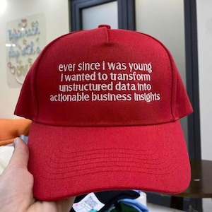 May include: A red baseball cap with white embroidered text. The text reads: "ever since I was young I wanted to transform unstructured data into actionable business insights."