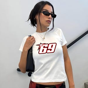 May include: White t-shirt featuring a red and white graphic of the number 69 with a star. The number is in a racing style font.