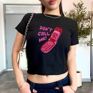 Könnte beinhalten: Schwarzes, bauchfreies T-Shirt mit einem pinkfarbenen Aufdruck eines Klapphandys und dem Text "Don't Call Me!"