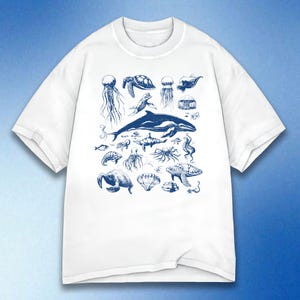 以下が含まれることがあります： クジラ、クラゲ、カメなど、さまざまな海の生き物を青色で描いたイラストが特徴の白いTシャツ。 海の生き物が好きな方にぴったりの、詳細で芸術的なデザインです。