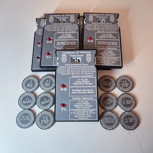 May include: A collection of gray game tokens and card-like pieces with white text and symbols. The pieces are labeled with phrases like "Leagues of Votann", "Yield Points", and "Re-Roll Advance". Some tokens have "+1 Hit" and "+1 Wound" printed on them.