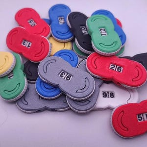 May include: A collection of colorful, oval-shaped game tokens. Each token is a different color, including red, blue, green, yellow, gray, black, and white. Each token has a number displayed in a small window.
