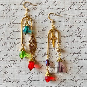 Puede incluir: Pendientes colgantes dorados con cuentas facetadas de colores y filigranas decorativas. Un pendiente presenta un dije de estrella, mientras que el otro tiene una cuenta turquesa y verde. Los pendientes tienen una est&eacute;tica vintage.
