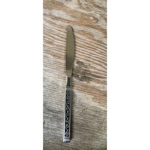 May include: A silver dinner knife with a black, ornate handle. The handle has a repeating pattern of swirls.