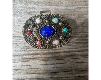 May include: An oval-shaped metal belt buckle with a blue, red, green, and white stone design.