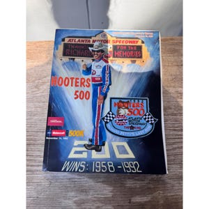 Puede incluir: Una portada de programa conmemorativo de la carrera Hooters 500 de 1992 en el Atlanta Motor Speedway. La portada presenta un retrato de Richard Petty, el piloto de carreras, con su traje de carreras. El programa conmemora la última carrera de Richard Petty.