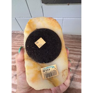 K&ouml;nnte beinhalten: Eine rechteckige, cremefarbene Steinskulptur mit schwarzem, kreisf&ouml;rmigem Sockel. Der Stein hat gelbe und braune Maserungen. Zwei Preisschilder sind an der Skulptur angebracht.