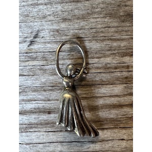 May include: Silver charm featuring a stylized figure of a woman holding a hoop.
