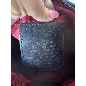 May include: A close-up of a black leather handbag tag with the text "C410162" and "Brighton". The tag also includes the text "The Brighton Collection handbags are individually crafted in China from quality leathers!"