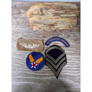 May include: A collection of four embroidered military patches including a tan rectangular patch with white wings, a blue arc patch reading AIR TRANSPORT COMMAND, a blue circular patch with orange wings and a star, and a black chevron rank patch.