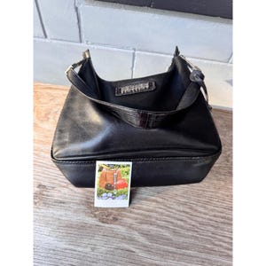 May include: Black leather shoulder bag with a rectangular base and a curved top. The bag has a short handle and a small, decorative crocodile-textured accent. A small photo with bags is visible.
