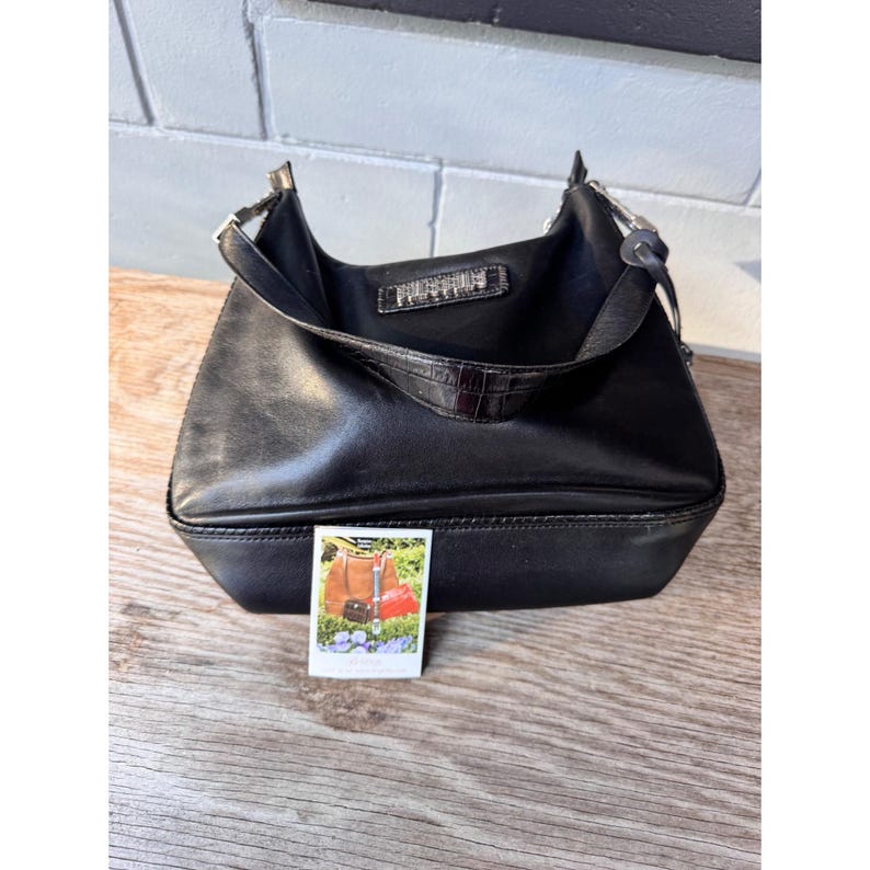 May include: Black leather shoulder bag with a rectangular base and a curved top. The bag has a short handle and a small, decorative crocodile-textured accent. A small photo with bags is visible.