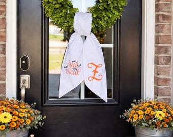Puede incluir: Una puerta principal negra decorada para Halloween con una corona verde, una pancarta de tela blanca con el texto "trick or treat" y una letra naranja "Z". Calabazas y crisantemos en cubos galvanizados flanquean la puerta, con una alfombra de bienvenida.