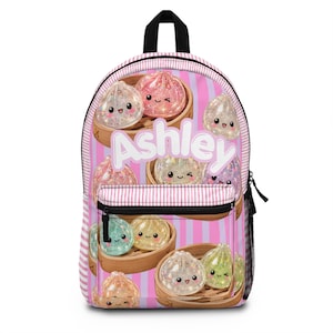 May include: A pink and white striped backpack featuring a repeating pattern of cute, glittery, cartoon-style dumplings in bamboo steamers. The name Ashley is printed in large white letters across the center of the bag, which has a black zipper.