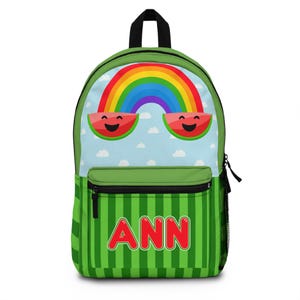 May include: Green backpack with a watermelon and rainbow design. The top section features a rainbow over a light blue sky with smiling watermelon slices. The bottom has green vertical stripes with the name "ANN" in red.