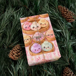 Könnte beinhalten: Eine rechteckige Geschenkbox, eingewickelt in hellrosa Papier mit einem Muster aus lächelnden Knödel-Illustrationen in Bambusdämpfern, zusammengebunden mit dünner Schnur. Die Knödel zeigen verschiedene Pastellfarben wie Rosa, Lila und Blau.