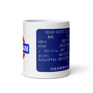 May include: White ceramic mug with a blue and red Nissan logo on the side. The mug features a blue rectangle with white text and Japanese characters. The text includes "NISSAN MOTOR CO" and "MODEL".