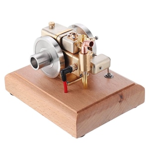 May include: A miniature model engine, featuring a brass and silver-colored design, mounted on a rectangular wooden base. The engine has a flywheel, pipes, and various mechanical components. The base is made of light brown wood.