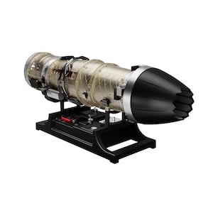 Puede incluir: Modelo detallado de un motor a reacción con una carcasa transparente que revela los componentes internos. El motor tiene un cono de morro negro y está montado sobre un soporte negro. Detalles plateados y palancas rojas.