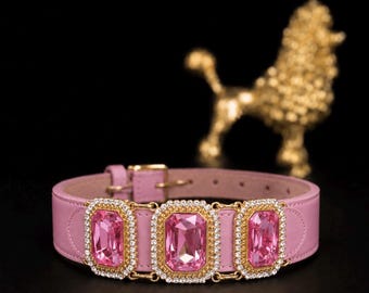 Puede incluir: Un collar de cuero rosa claro con tres grandes cristales rosas rectangulares facetados en monturas de metal dorado. Cada cristal está rodeado por un borde de pequeños diamantes de imitación transparentes y brillantes. El collar incluye una hebilla dorada.