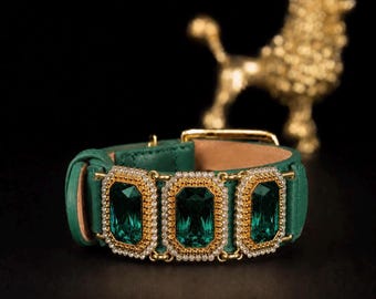 Puede incluir: Una pulsera de cuero verde con tres grandes cristales facetados de color verde esmeralda en forma rectangular. Cada cristal está enmarcado por un borde de pequeñas piedras claras brillantes y un engaste de metal dorado. Incluye una hebilla dorada.