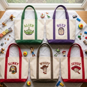 May include: Five off-white canvas tote bags with colored handles and bases. Each bag features an embroidered character face and name: Alien with green trim, Buzz with purple trim, Slinky with red trim, Woody with brown trim, and Jessie with red trim.