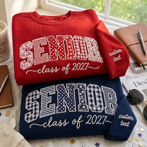 Könnte beinhalten: Ein rotes Sweatshirt und ein marineblaues Sweatshirt, jeweils mit dem Wort SENIOR in großen, gemusterten Blockbuchstaben und dem darunter gestickten Text class of 2027. Jeder Ärmel trägt den gestickten Text custom text.