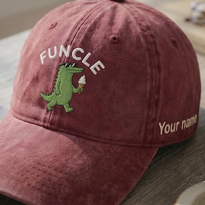 May include: A maroon baseball cap featuring an embroidered green alligator wearing black sunglasses and holding an ice cream cone. The word "FUNCLE" is embroidered in white above the alligator, and the text "Your name" appears on the side.