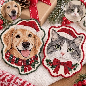 May include: Two embroidered patches featuring a golden retriever wearing a red and green plaid scarf and a grey and white cat with a red bow, both wearing red Santa hats with white trim, set against a cream-colored fabric background.