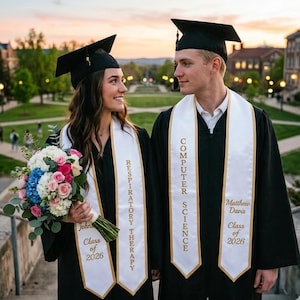 May include: Two graduates in black gowns and mortarboards, smiling at each other. One holds a bouquet of flowers. White stoles with gold lettering read "Respiratory Therapy" and "Computer Science." The text "Class of 2026" is also visible.