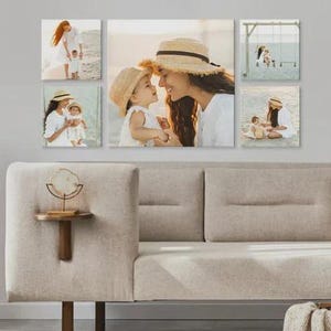 Pu&ograve; includere: Un'esposizione di arte murale con sei stampe su tela di una madre e un bambino. Le stampe mostrano la coppia su una spiaggia, con cappelli di paglia e abiti bianchi. Le stampe sono montate sopra un divano beige.