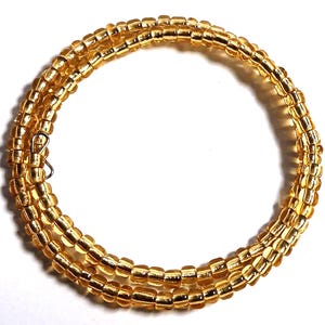 Puede incluir: Un collar enrollado hecho de peque&ntilde;as cuentas de color amarillo dorado. El collar est&aacute; envuelto en m&uacute;ltiples hebras y asegurado con un peque&ntilde;o cierre plateado. Las cuentas tienen una apariencia ligeramente transl&uacute;cida, y el dise&ntilde;o es simple y elegante.