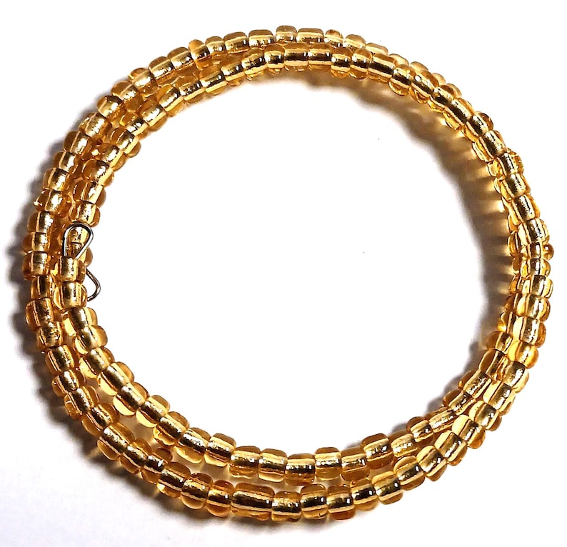 Puede incluir: Un collar enrollado hecho de peque&ntilde;as cuentas de color amarillo dorado. El collar est&aacute; envuelto en m&uacute;ltiples hebras y asegurado con un peque&ntilde;o cierre plateado. Las cuentas tienen una apariencia ligeramente transl&uacute;cida, y el dise&ntilde;o es simple y elegante.