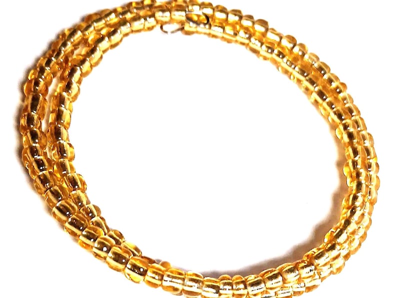 Puede incluir: Un collar de cuentas doradas con un dise&ntilde;o en espiral. El collar est&aacute; hecho de peque&ntilde;as cuentas redondas y tiene un cierre de broche. Las cuentas son de un color &aacute;mbar c&aacute;lido y reflejan la luz.