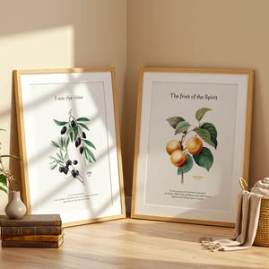 Può includere: Due stampe botaniche incorniciate con cornici in legno chiaro. Una presenta un ramo d'ulivo con il testo "Io sono la vite". L'altra stampa mostra albicocche e il testo "Il frutto dello Spirito".