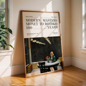 May include: A framed art print featuring the text "MODERN MASTERS MONET TO ROTHKO 100 YEARS" from the Musée d'Orsay, Paris. The artwork depicts a woman in a green coat and hat seated at a table in a diner. The frame is a light brown color.
