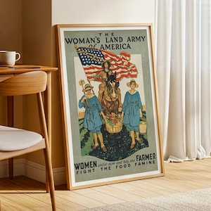 May include: Framed vintage poster with the text "THE WOMAN'S LAND ARMY of AMERICA." The poster features an illustration of women in blue outfits and straw hats, with an American flag and a horse. The text "WOMEN enlist now and help the FARMER FIGHT THE FOOD FAMINE" is also included.
