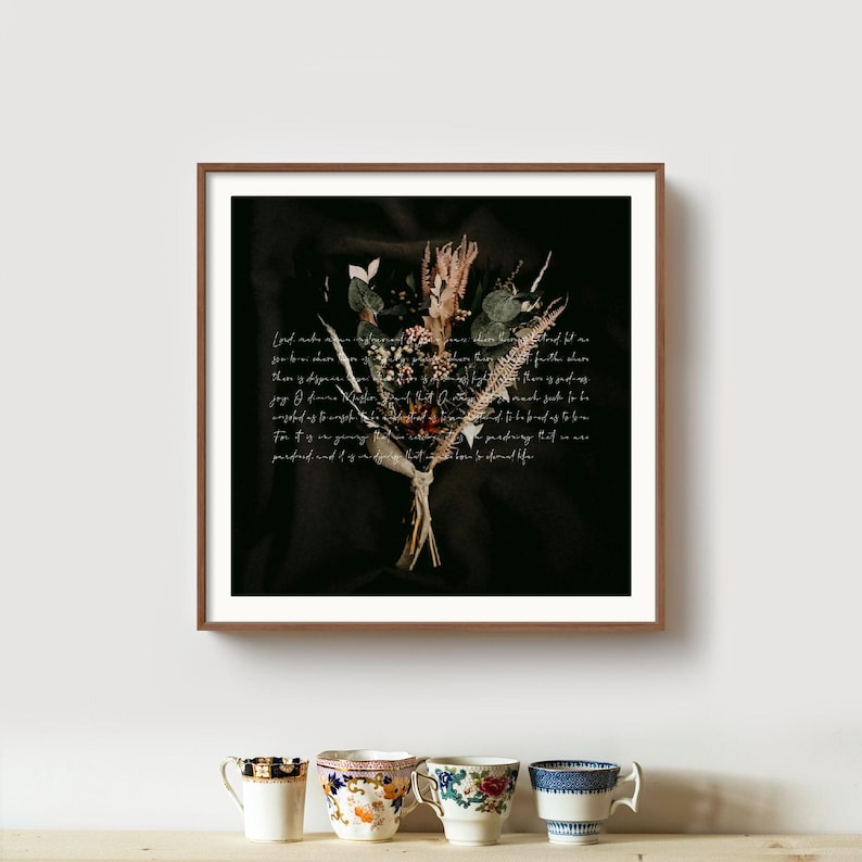 May include: A framed print featuring a dried flower bouquet against a dark background. The bouquet includes various dried flowers and greenery, tied together with twine. Handwritten script is overlaid on the dark background. The frame is a dark brown color.