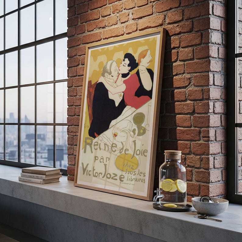 May include: A framed vintage poster titled "Reine de Joie" by Victor Joze, featuring a colorful illustration of figures in a cafe setting. The poster is displayed on a windowsill with a brick wall backdrop, alongside a glass water dispenser and books.