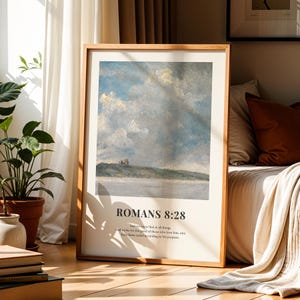 Könnte beinhalten: Ein gerahmter Kunstdruck mit einer Landschaftsmalerei mit bewölktem Himmel und Wasser. Der Druck hat den Text "ROMANS 8:28" und einen Bibelvers auf hellem Hintergrund. Der Rahmen ist aus hellem Holz.