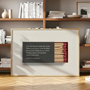 May include: Framed art print with a matchbox design and a quote by Hunter S. Thompson. The quote, in white text on a dark grey background, reads "Buy the ticket, take the ride." The matchsticks have red tips.
