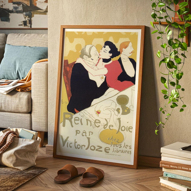 May include: A framed vintage poster with a wooden frame. The poster features an illustration of three people, with the text "Reine de Joie par Victor Joze" in yellow and black. Brown leather sandals are on the floor.