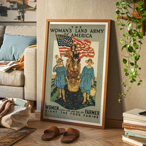 May include: A framed vintage poster with a wooden frame. The poster features an illustration of women in blue uniforms and straw hats, with an American flag and a horse. The text reads "The Woman's Land Army of America" and "Women enlist now and help the Farmer fight the food famine."